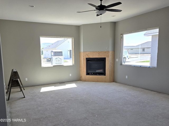 unfurnished living room featuring ceiling fan and a glass covered fireplace