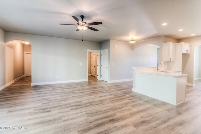 unfurnished living room featuring arched walkways, light wood-style flooring, a sink, ceiling fan, and baseboards