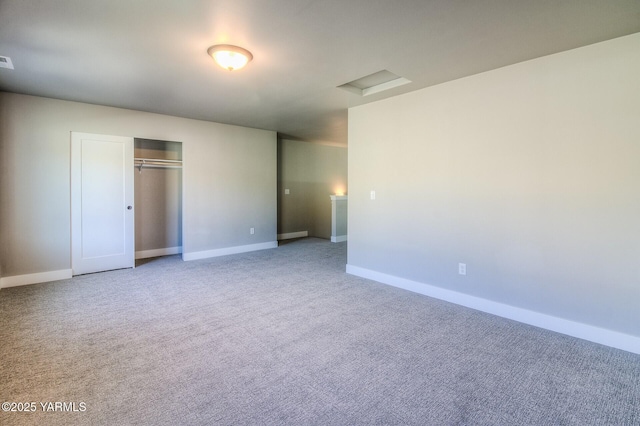 unfurnished bedroom with carpet floors, a closet, attic access, and baseboards