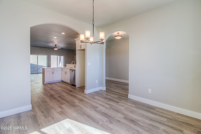 kitchen featuring white cabinets, decorative light fixtures, light countertops, stainless steel dishwasher, and a sink