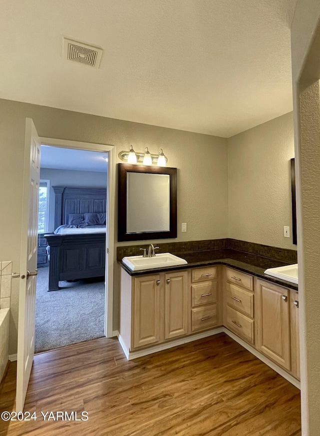 full bathroom with ensuite bathroom, a textured wall, wood finished floors, vanity, and visible vents