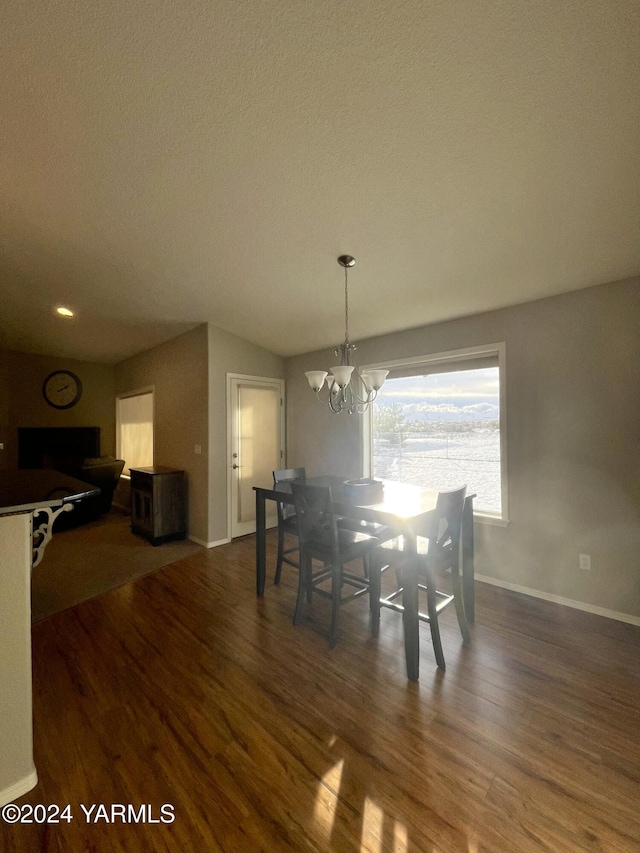 dining area with dark wood-style floors, a textured ceiling, baseboards, and a notable chandelier