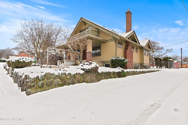 snow covered property featuring a chimney, fence, and a balcony