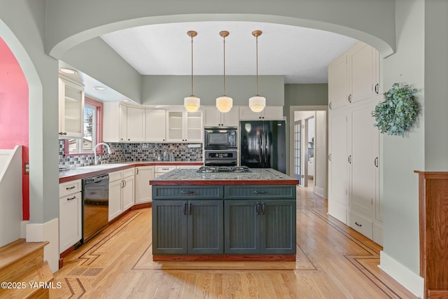 kitchen featuring a kitchen island, glass insert cabinets, decorative light fixtures, black appliances, and white cabinetry