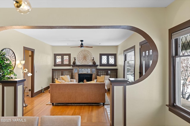 living area featuring ceiling fan, arched walkways, a fireplace, baseboards, and light wood-style floors