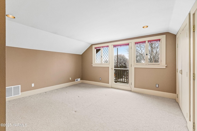 additional living space featuring light colored carpet, visible vents, vaulted ceiling, and baseboards