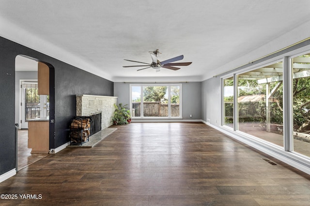 118 Glen Dr, Zillah, WA 98953 - unfurnished living room featuring a ceiling fan, wood finished floors, a fireplace with raised hearth, and arched walkways