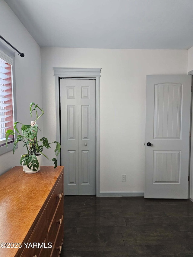 unfurnished bedroom with dark wood-type flooring, a closet, and baseboards