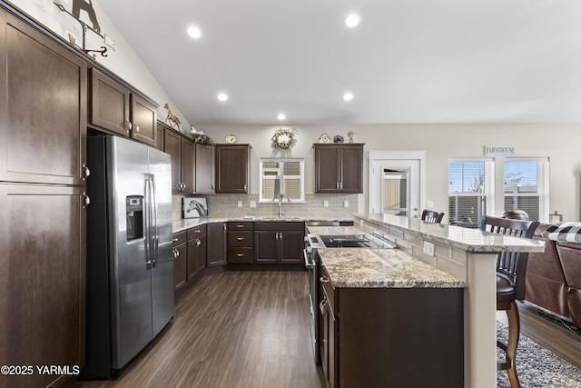 kitchen featuring a breakfast bar, dark brown cabinets, appliances with stainless steel finishes, decorative backsplash, and a center island