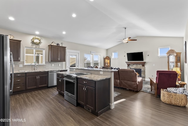 kitchen featuring dark wood finished floors, a fireplace, stainless steel appliances, open floor plan, and dark brown cabinets