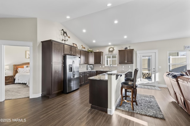 kitchen with dark brown cabinetry, stainless steel fridge, lofted ceiling, a breakfast bar, and backsplash