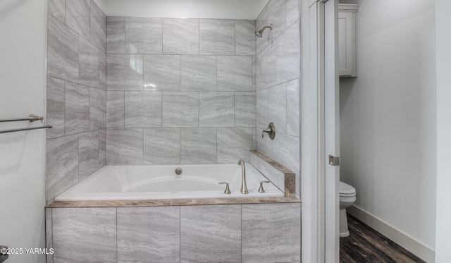 bathroom with tiled shower / bath combo, toilet, baseboards, and wood finished floors