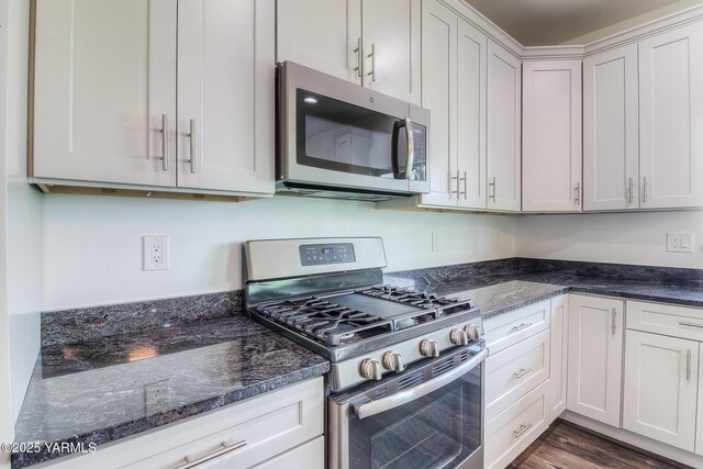 kitchen with dark wood-style floors, white cabinetry, stainless steel appliances, and dark stone counters