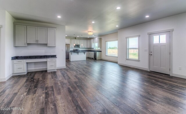 kitchen featuring dark countertops, built in study area, stainless steel appliances, and dark wood-style flooring