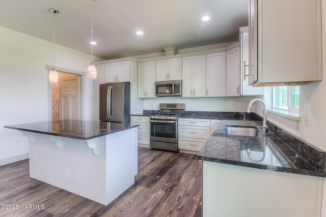 kitchen featuring a sink, a kitchen island, dark wood-style floors, stainless steel appliances, and a breakfast bar area