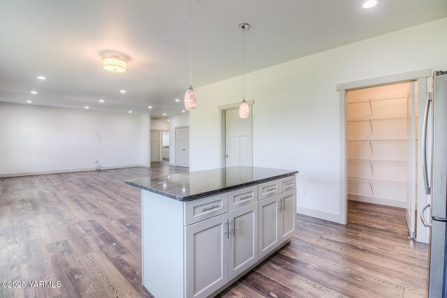 kitchen featuring recessed lighting, dark stone countertops, freestanding refrigerator, wood finished floors, and hanging light fixtures