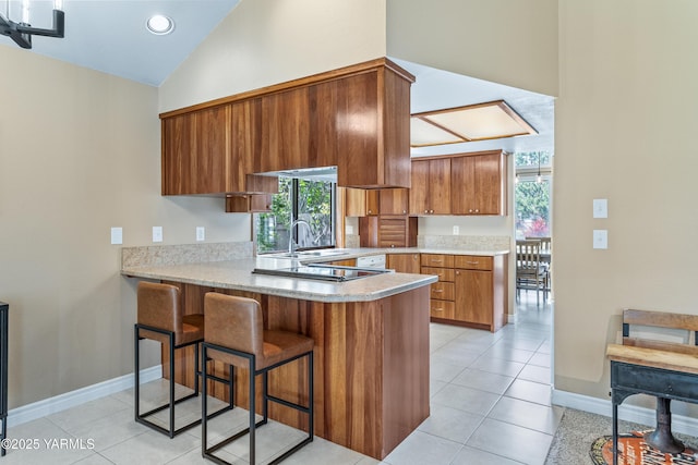 5504 Webster Ave, Yakima, WA 98908 - kitchen with brown cabinetry, a peninsula, light countertops, a breakfast bar area, and light tile patterned floors