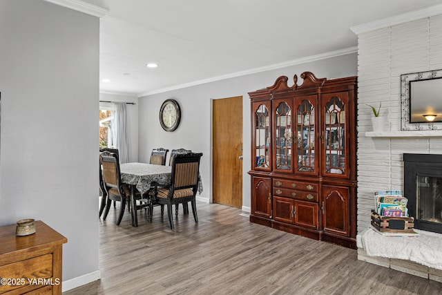 dining space featuring baseboards, wood finished floors, a brick fireplace, and ornamental molding