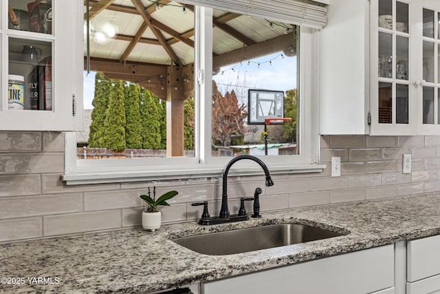 kitchen featuring a sink, glass insert cabinets, tasteful backsplash, and white cabinets