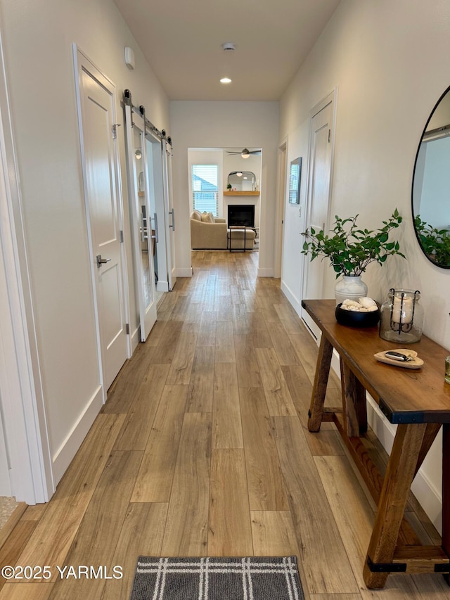 hallway with baseboards, light wood-style floors, and a barn door