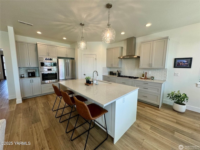 kitchen featuring wall chimney exhaust hood, decorative light fixtures, stainless steel appliances, light countertops, and a sink