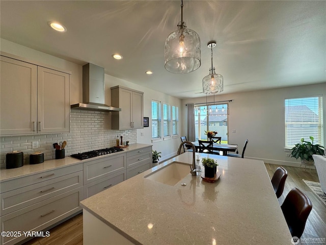 kitchen featuring wall chimney exhaust hood, black gas cooktop, gray cabinets, pendant lighting, and a sink