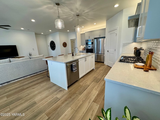 kitchen featuring decorative light fixtures, a center island with sink, stainless steel appliances, open floor plan, and a sink