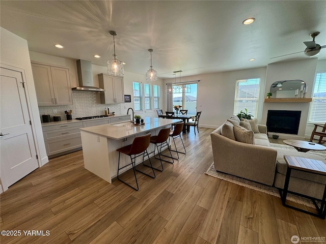 kitchen with a center island with sink, wall chimney exhaust hood, a breakfast bar area, hanging light fixtures, and light countertops