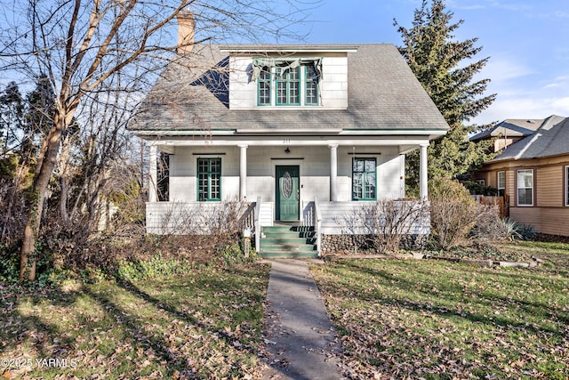 bungalow-style home with covered porch, roof with shingles, a chimney, and a front yard