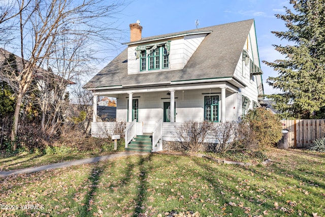 view of front of house with roof with shingles, a chimney, a porch, fence, and a front lawn