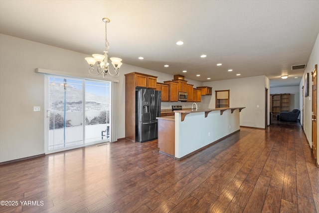 kitchen with brown cabinetry, appliances with stainless steel finishes, dark wood-style flooring, a kitchen bar, and pendant lighting