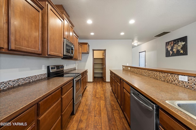 kitchen with tasteful backsplash, visible vents, dark countertops, dark wood-style floors, and stainless steel appliances