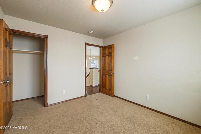 unfurnished bedroom with light carpet, a textured ceiling, baseboards, and a closet