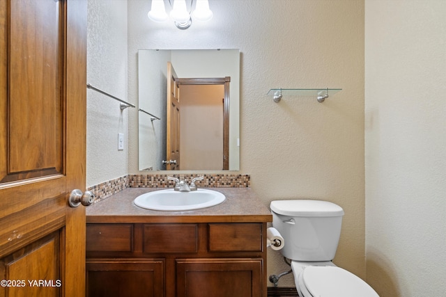 half bathroom featuring a textured wall, vanity, and toilet