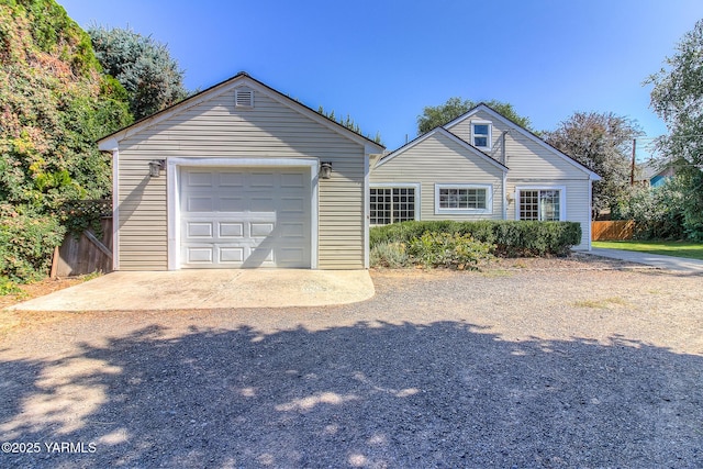 view of front of house with driveway, a detached garage, fence, and an outdoor structure