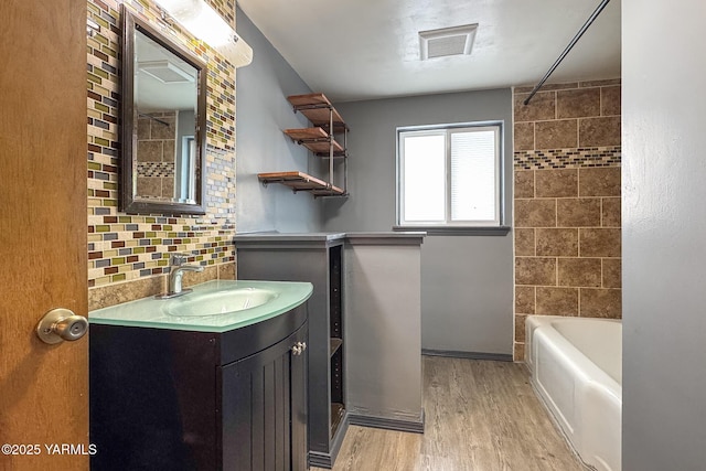 full bathroom with wood finished floors, visible vents, vanity, tub / shower combination, and tasteful backsplash