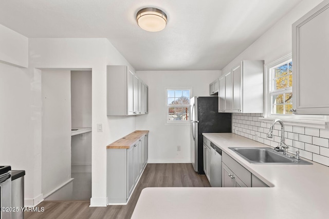 kitchen featuring dark wood-style floors, a sink, backsplash, and stainless steel dishwasher