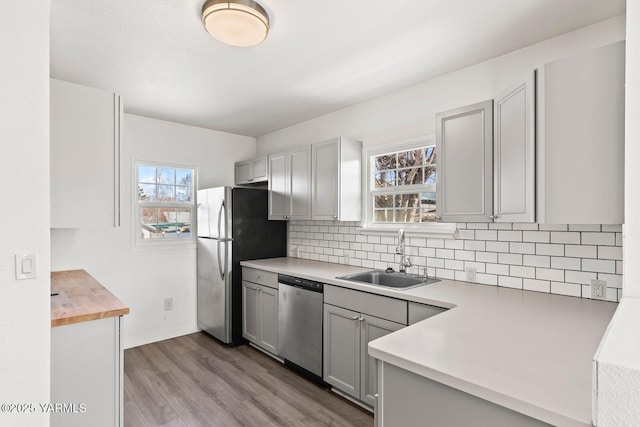 kitchen with gray cabinetry, stainless steel appliances, a sink, light wood-type flooring, and tasteful backsplash