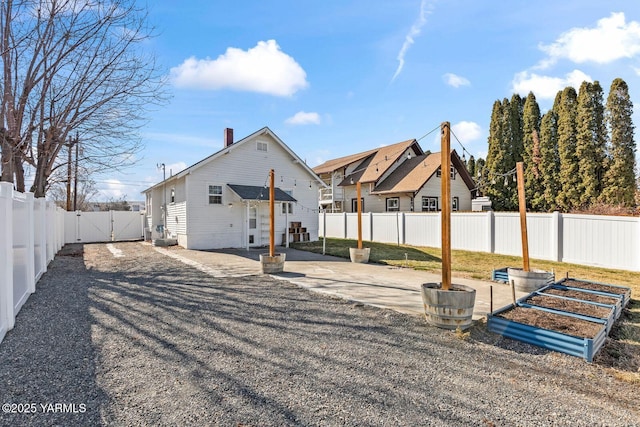 back of house with a fenced backyard, driveway, a gate, a chimney, and a patio area