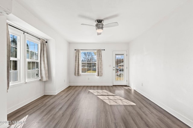 spare room featuring an AC wall unit, a healthy amount of sunlight, baseboards, and dark wood-style flooring