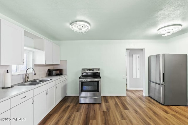 kitchen featuring stainless steel appliances, a sink, white cabinetry, light countertops, and dark wood finished floors