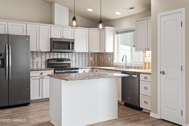 kitchen with white cabinets, a kitchen island, stainless steel appliances, and decorative light fixtures