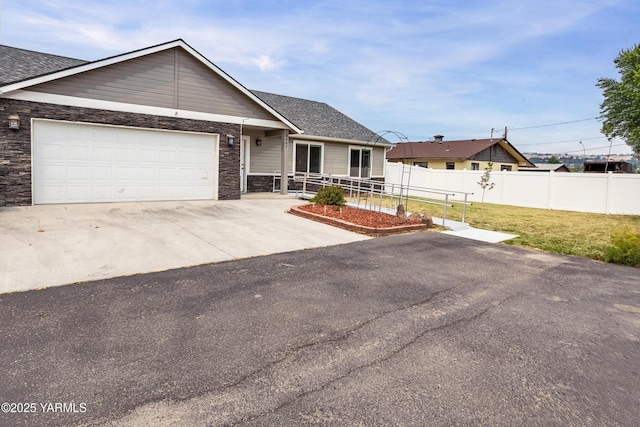 ranch-style house with concrete driveway, stone siding, an attached garage, fence, and a front yard