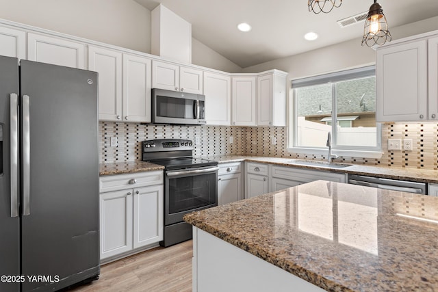 kitchen with light stone counters, stainless steel appliances, lofted ceiling, white cabinets, and a sink