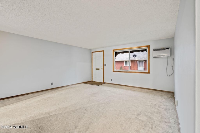 unfurnished room featuring baseboards, a wall mounted air conditioner, light carpet, and a textured ceiling