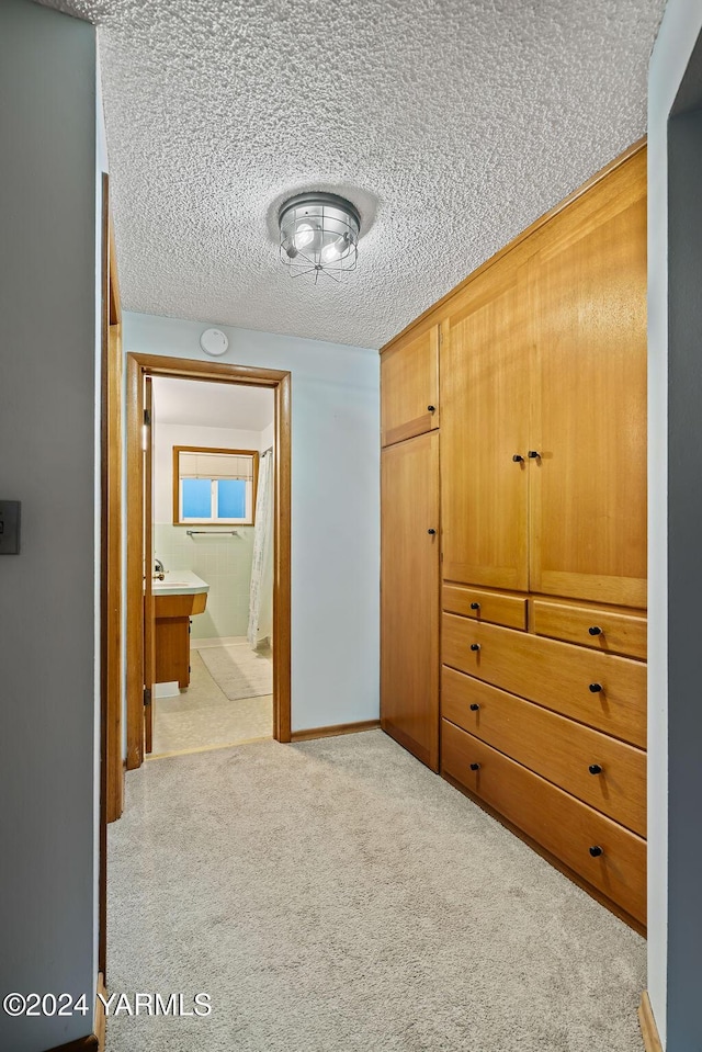 hall featuring light colored carpet, a textured ceiling, and baseboards