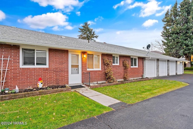 single story home with a shingled roof, a front lawn, and brick siding