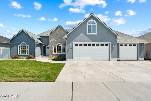 traditional-style house featuring stucco siding, an attached garage, a front yard, stone siding, and driveway