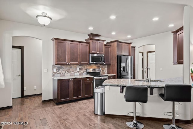 kitchen featuring arched walkways, light wood-style flooring, stainless steel appliances, a sink, and decorative backsplash