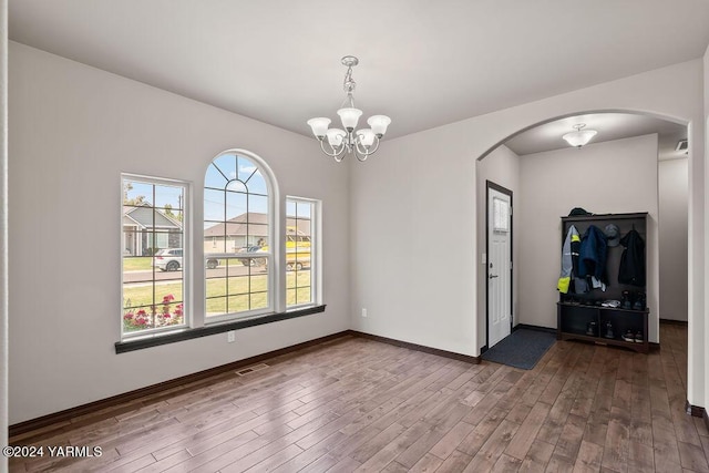 unfurnished room with arched walkways, a notable chandelier, wood finished floors, visible vents, and baseboards